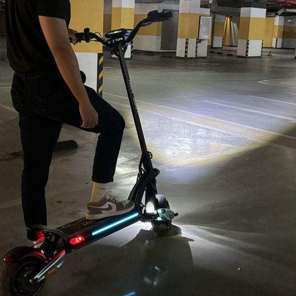 Un utilizator stă pe o trotinetă electrică iluminată într-o parcare subterană.